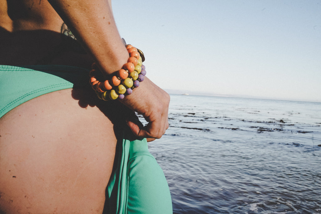 A close up detail shot of Alyssa holding her bikini top in one hand facing the ocean. 
