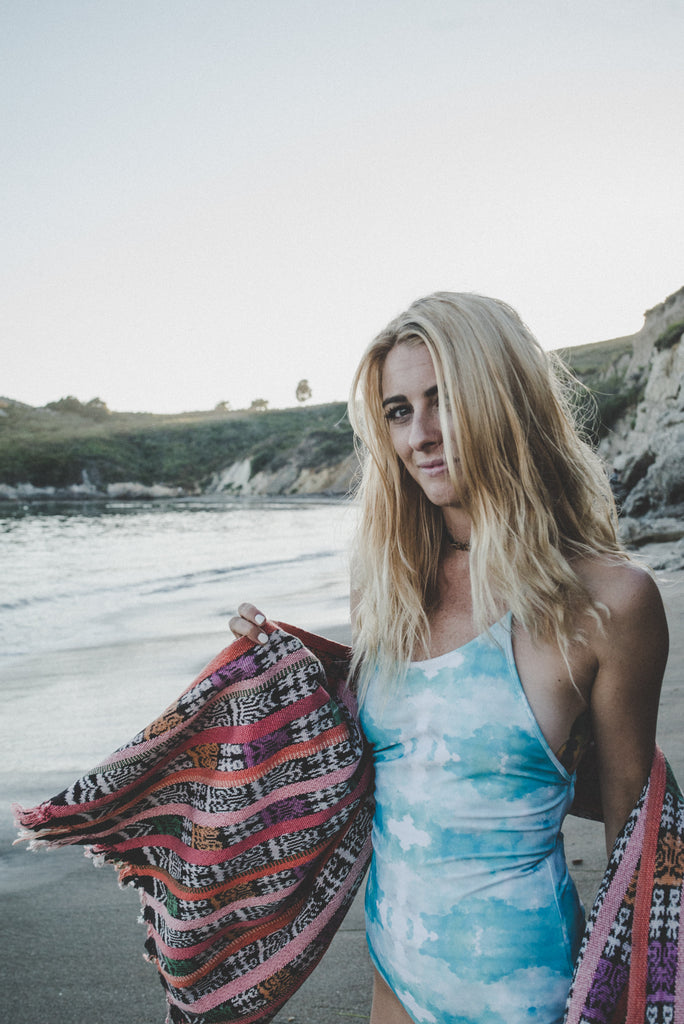 Alyssa holding a Hiptipico pink rebozo while facing the camera wearing a blue and white tie-dye one piece swimsuit.