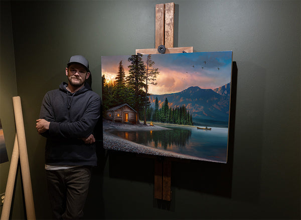 Artist Chuck Black with oil painting of lake cabin