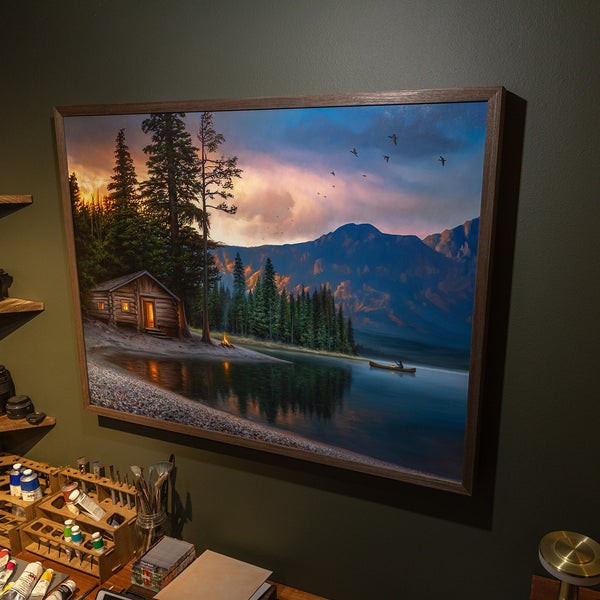 Framed painting of lake cabin at sunrise