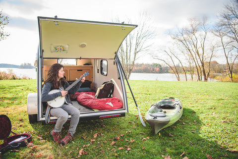 woman with banjo in a teardrop camper in the sun