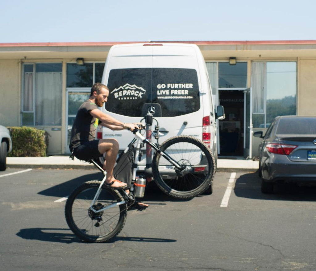 Person doing wheelie on bike wearing Bedrock Sandals in front of office