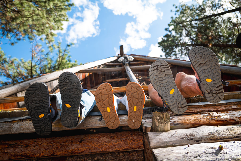 Three pairs of feet overhanging a cabin deck featuring Vibram soled Bedrock Sandals