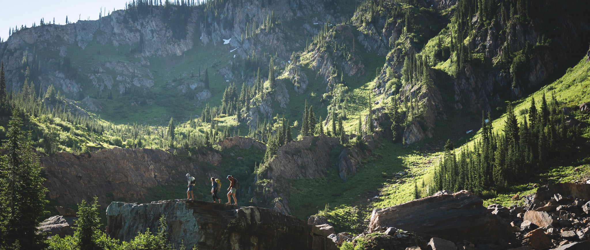 Three people hiking in the distance amidst mountains