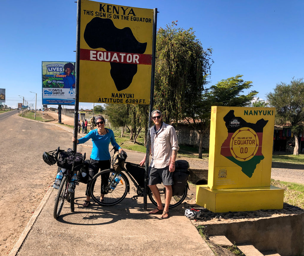 Two Cyclists standing next to an Equator sign