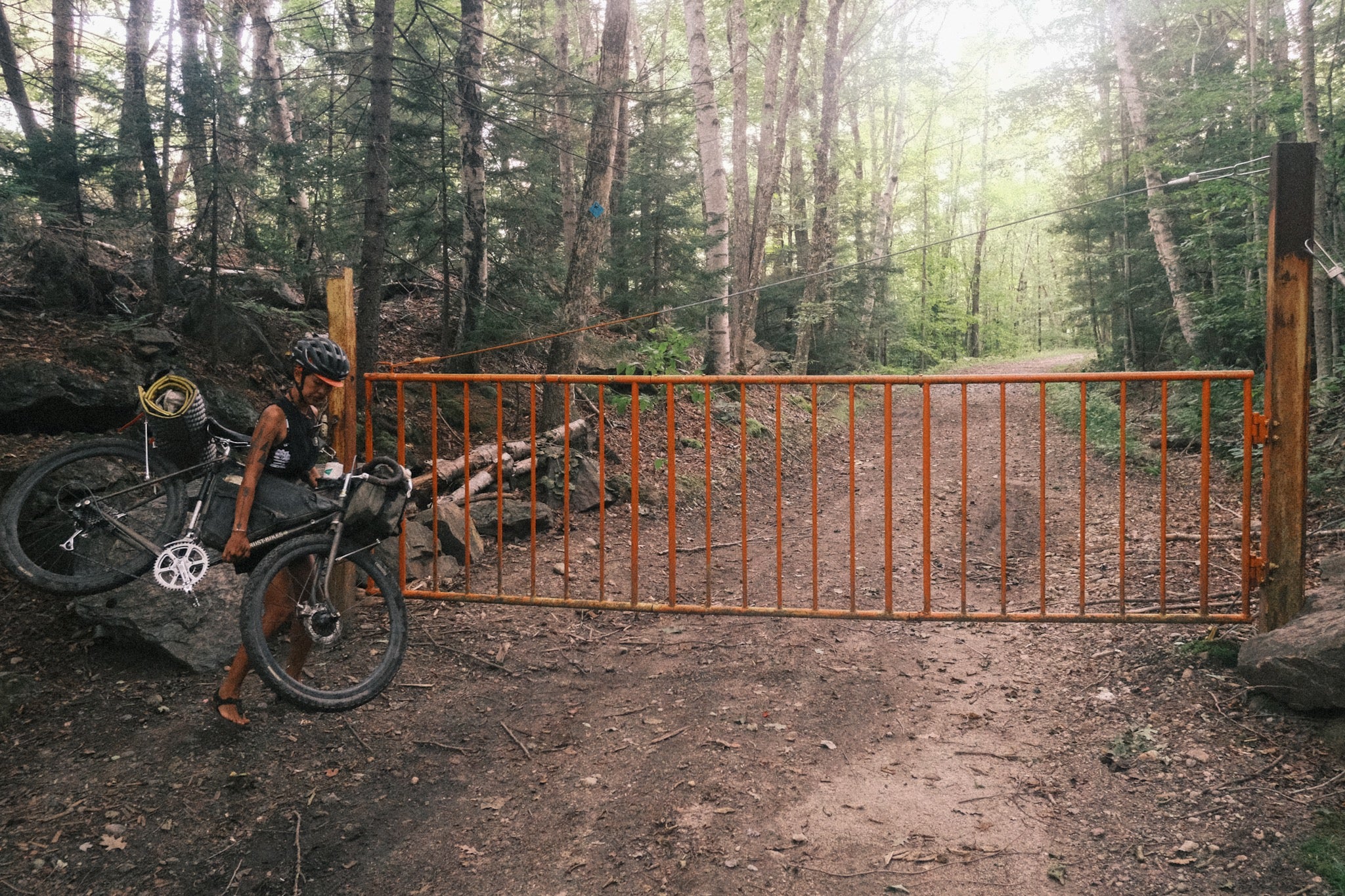 Lifting up their bike to cross a gated in a dirt road