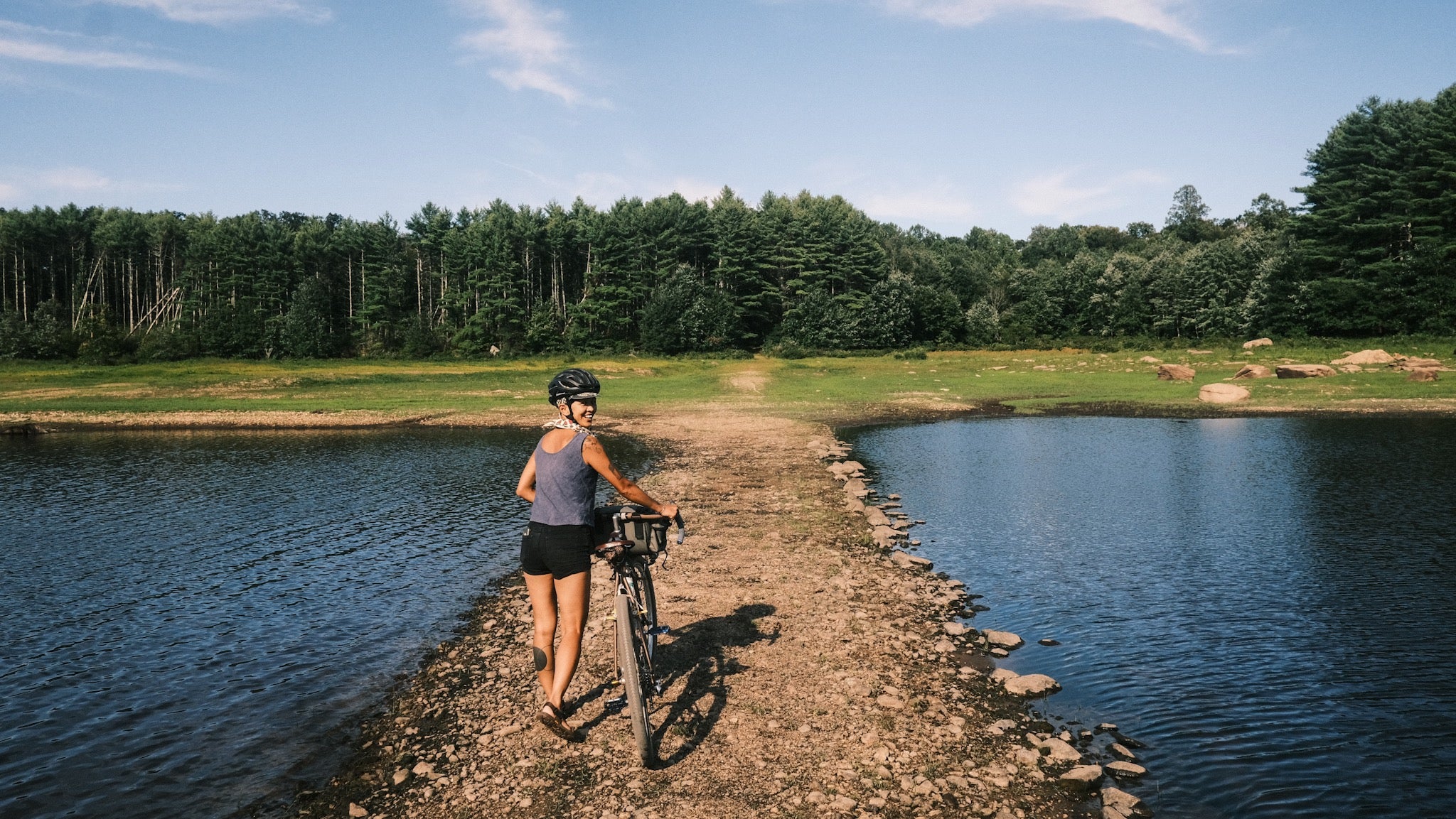 Walking their bike on a thin peninsula of land between ponds in New England