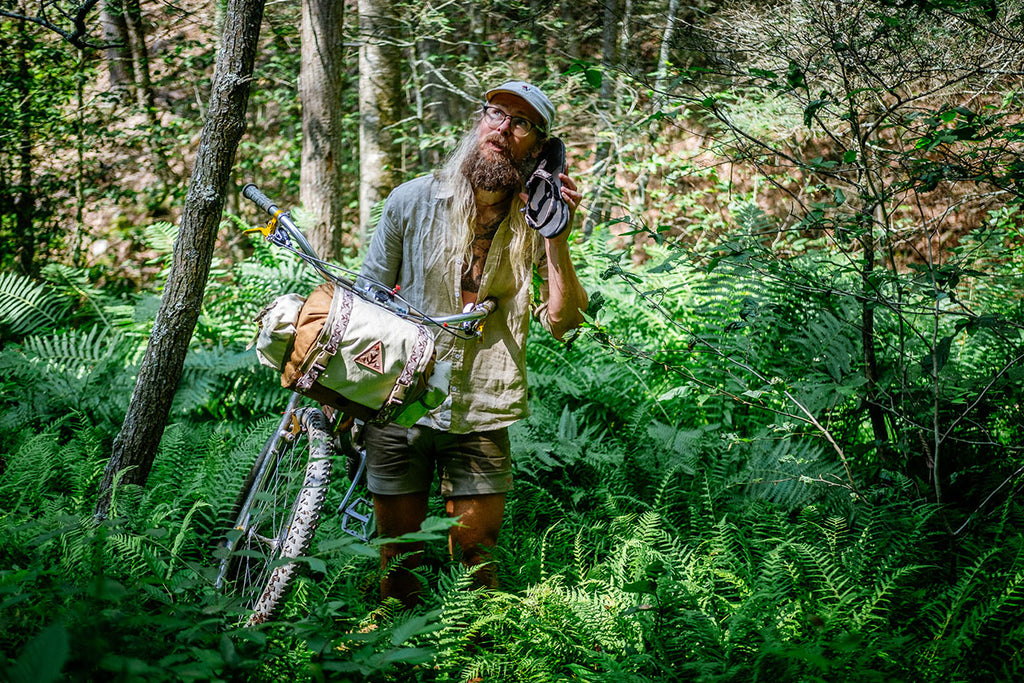 Ron's Bikes - Ronnie stands in a field using the sandal as a phone