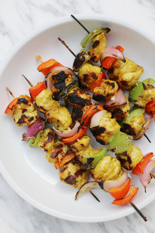 Curry chicken skewers with peppers and onions on a white plate