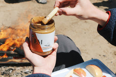 Dipping apple slice in JEM Organics nut butter by a fire pit