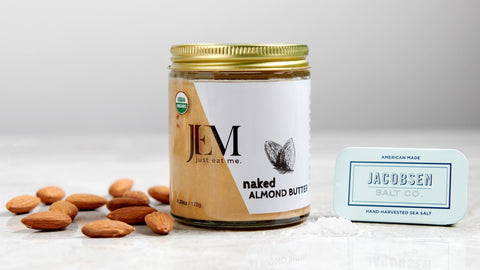 JEM Organics almond butter jar next to raw almonds and salt on a marble slab