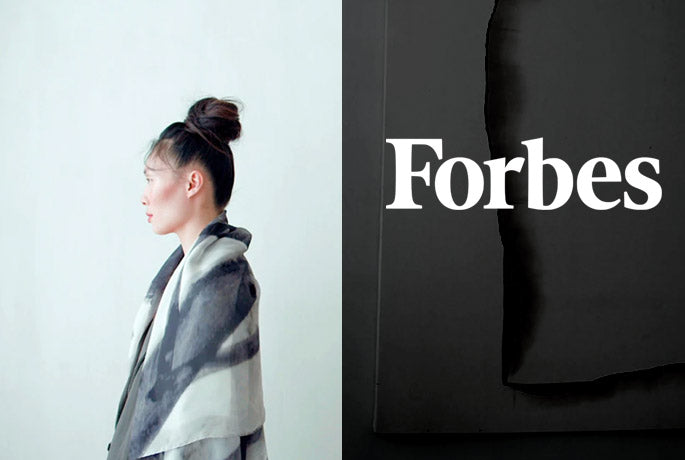 Forbes logo in white on textured dark background on the right, on the left a woman in profile with an Alba Amicorum Man Ray scarf draped over her shoulders in from of a pale softly lit wall