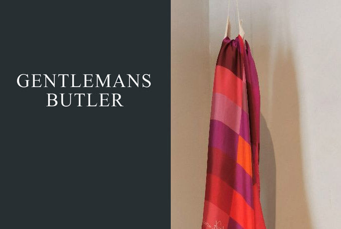 Gentlemans Butler logo in white on a dark gray background with a Darshana Shilpi Color Block scarf draped covering a dress form on the right