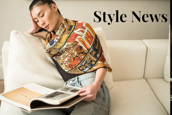 A woman lounges on a white couch, reading, and wearing an Alba Amicorum Indian Carousel luxury scarf - the Style News logo in black is superimposed above the couch