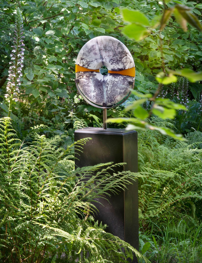 torus shaped marble sculpture mounted atop a wooden post in a lush garden