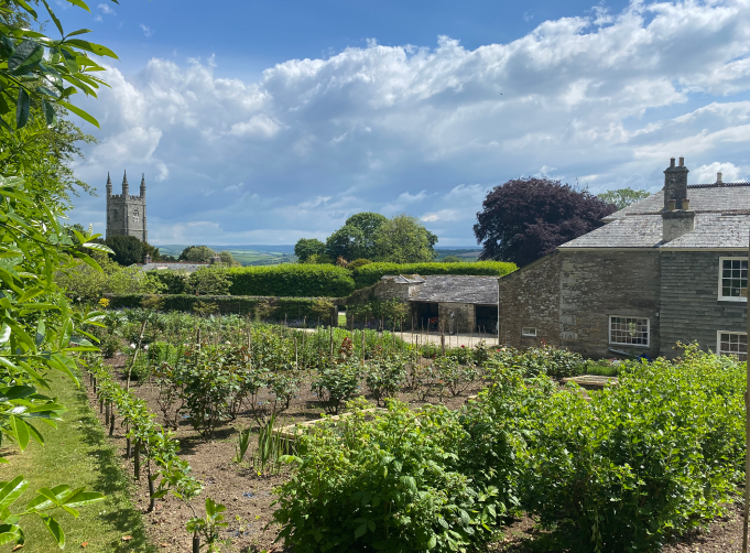 View of the manor and garden of Withiel - stone buildings and lush gardents - a beautiful blue sky with fluffy clouds