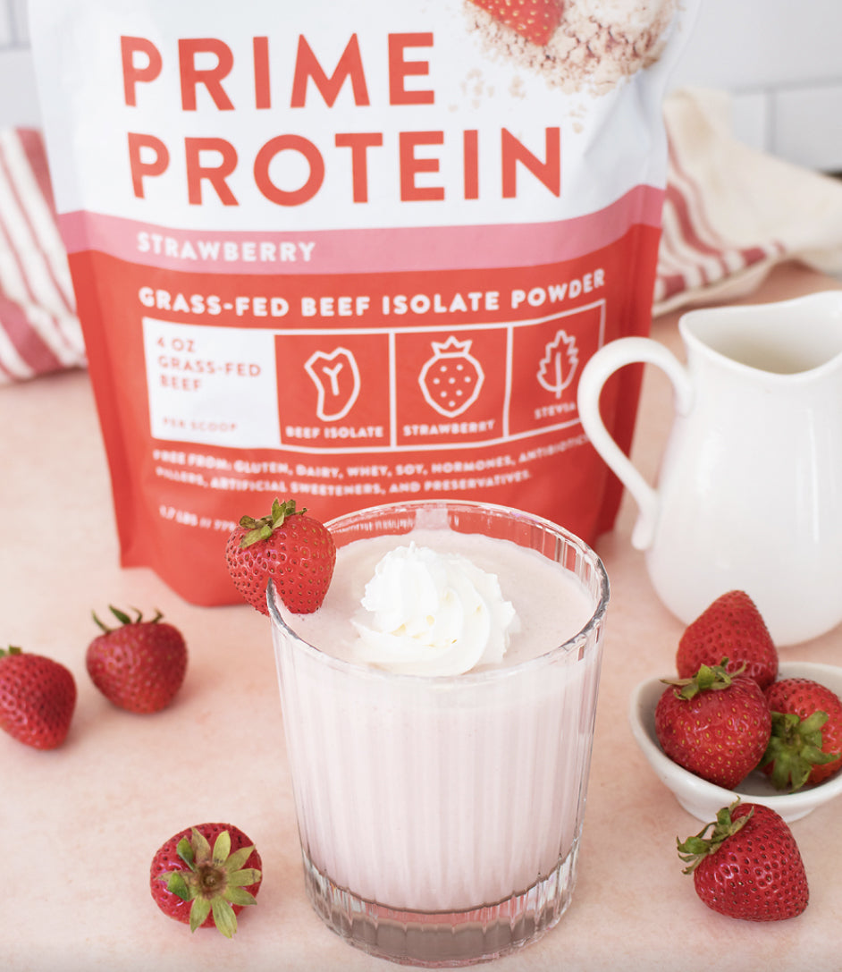 Strawberry protein powder with a strawberry smoothie topped with whipped cream, surrounded by whole strawberries.