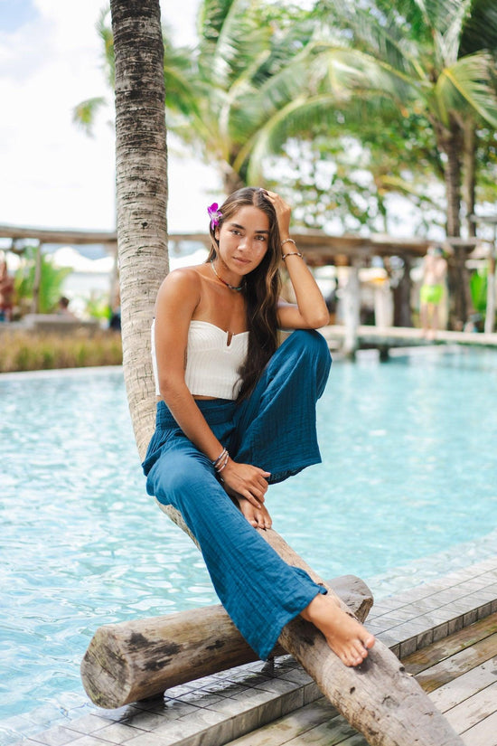 A woman is sitting on a palm tree in front of a pool