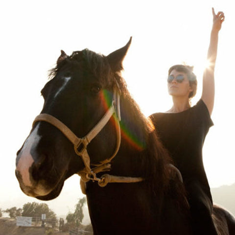 Cate Le Bon riding a horse with her arm up in the air 