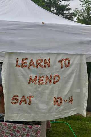 picture of a banner made from an old curtain and fabric scraps to encourage people to learn to mend and repair clothes