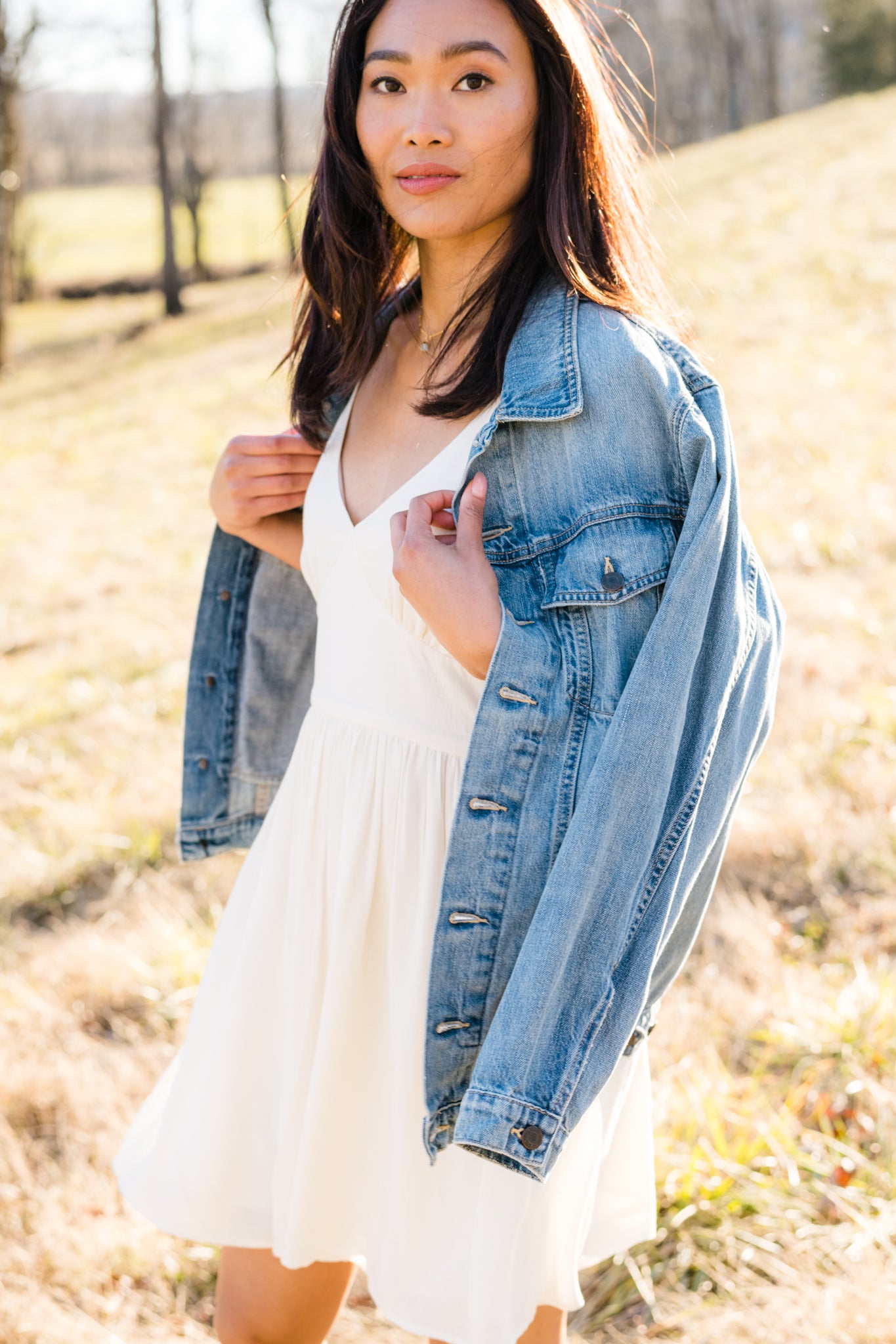 Woman in a white dress and denim jacket standing outdoors.