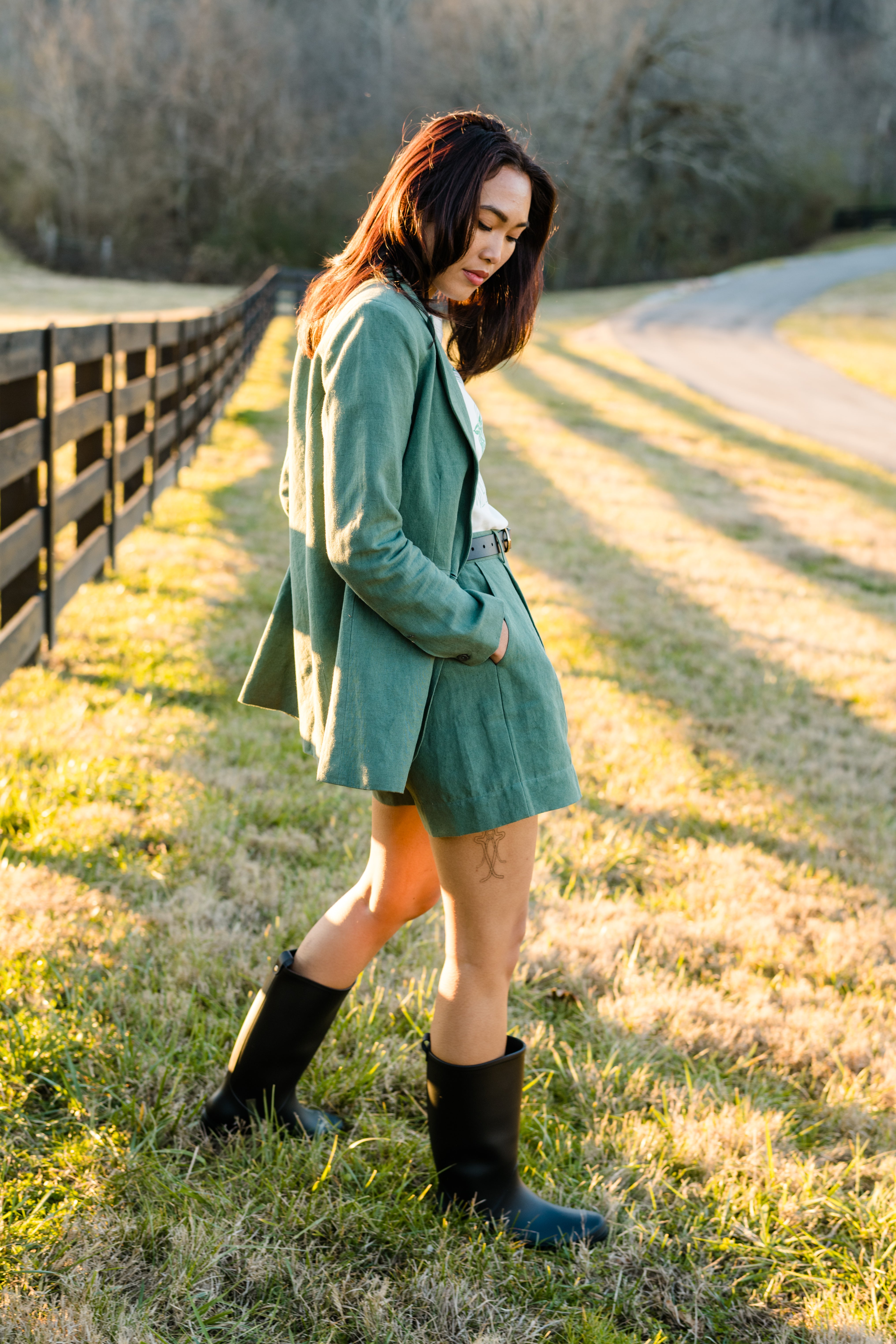 Woman in green outfit and black boots walking by a fence outdoors.
