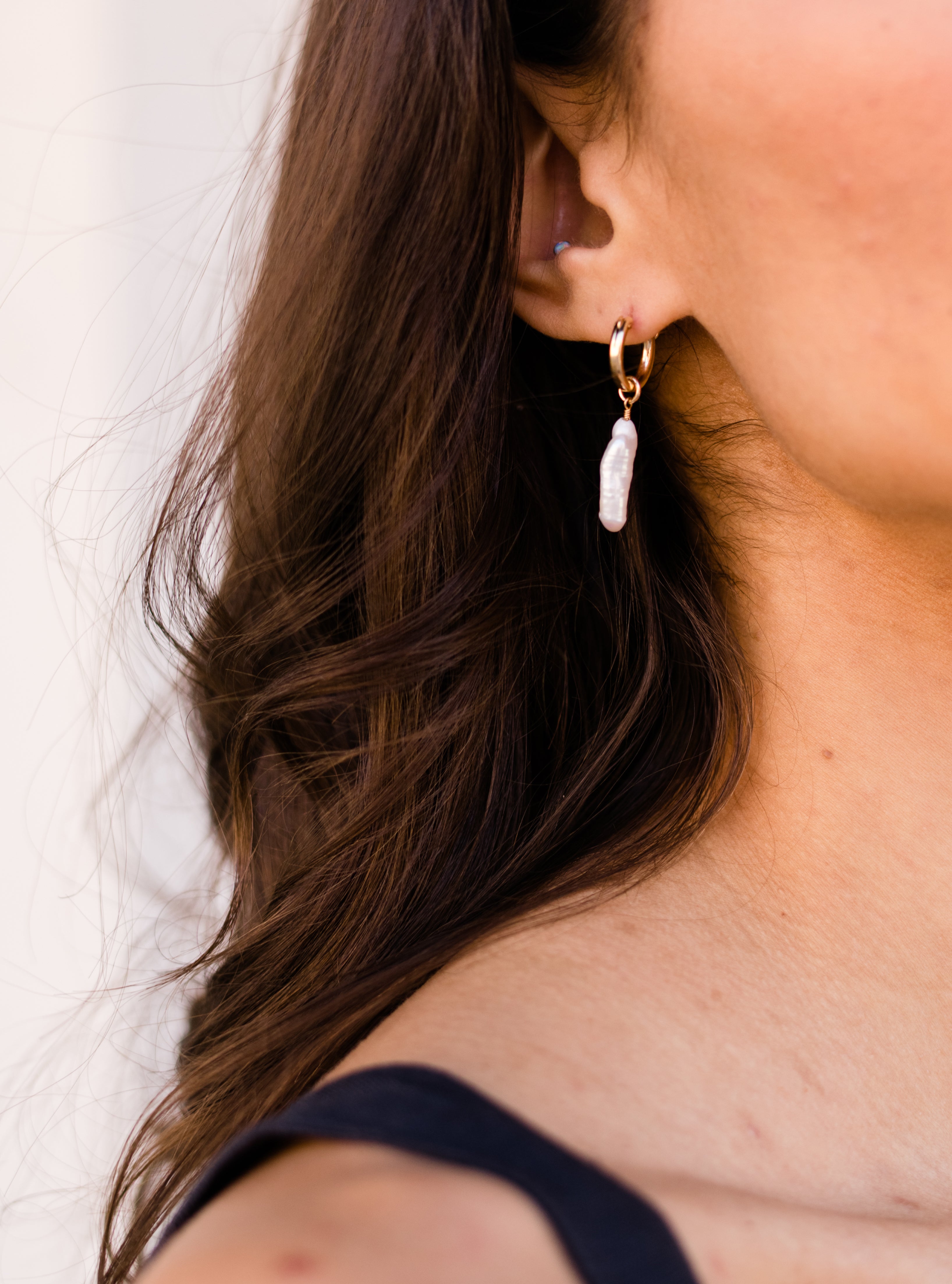Close-up of a woman's ear wearing a pearl earring, with dark flowing hair.