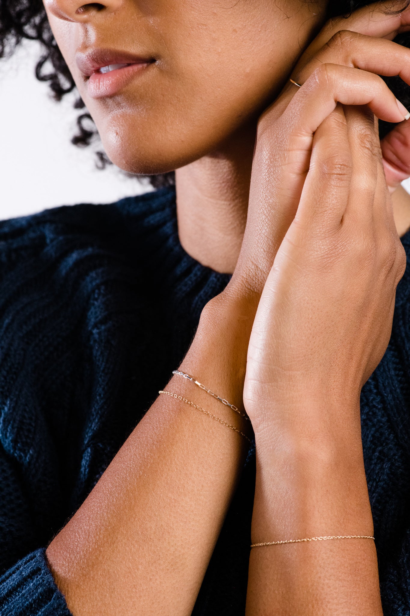 Close-up of a person wearing delicate gold bracelets and a dark knitted sweater.