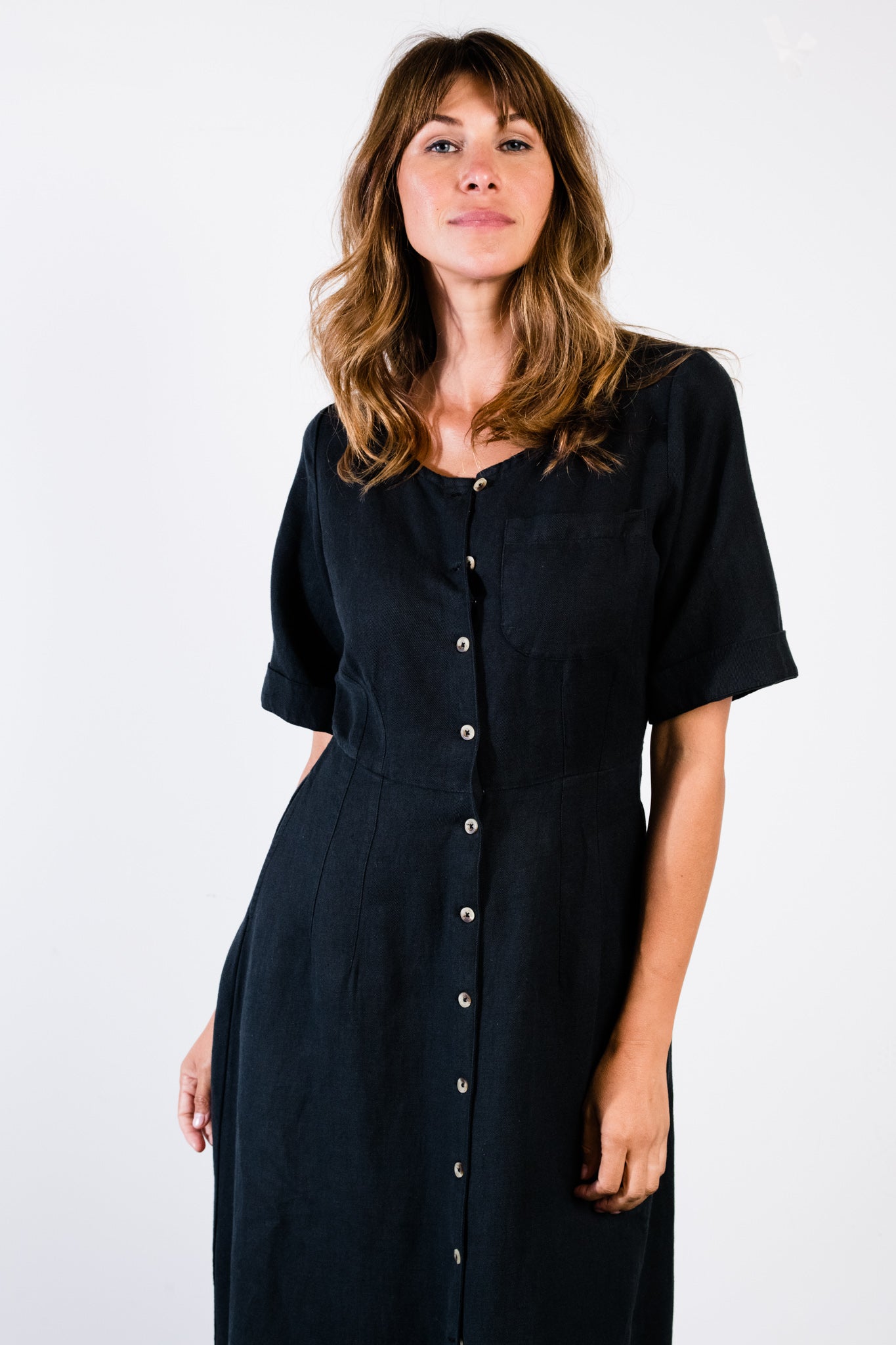 Woman wearing a black button-up dress with short sleeves, standing against a white background.