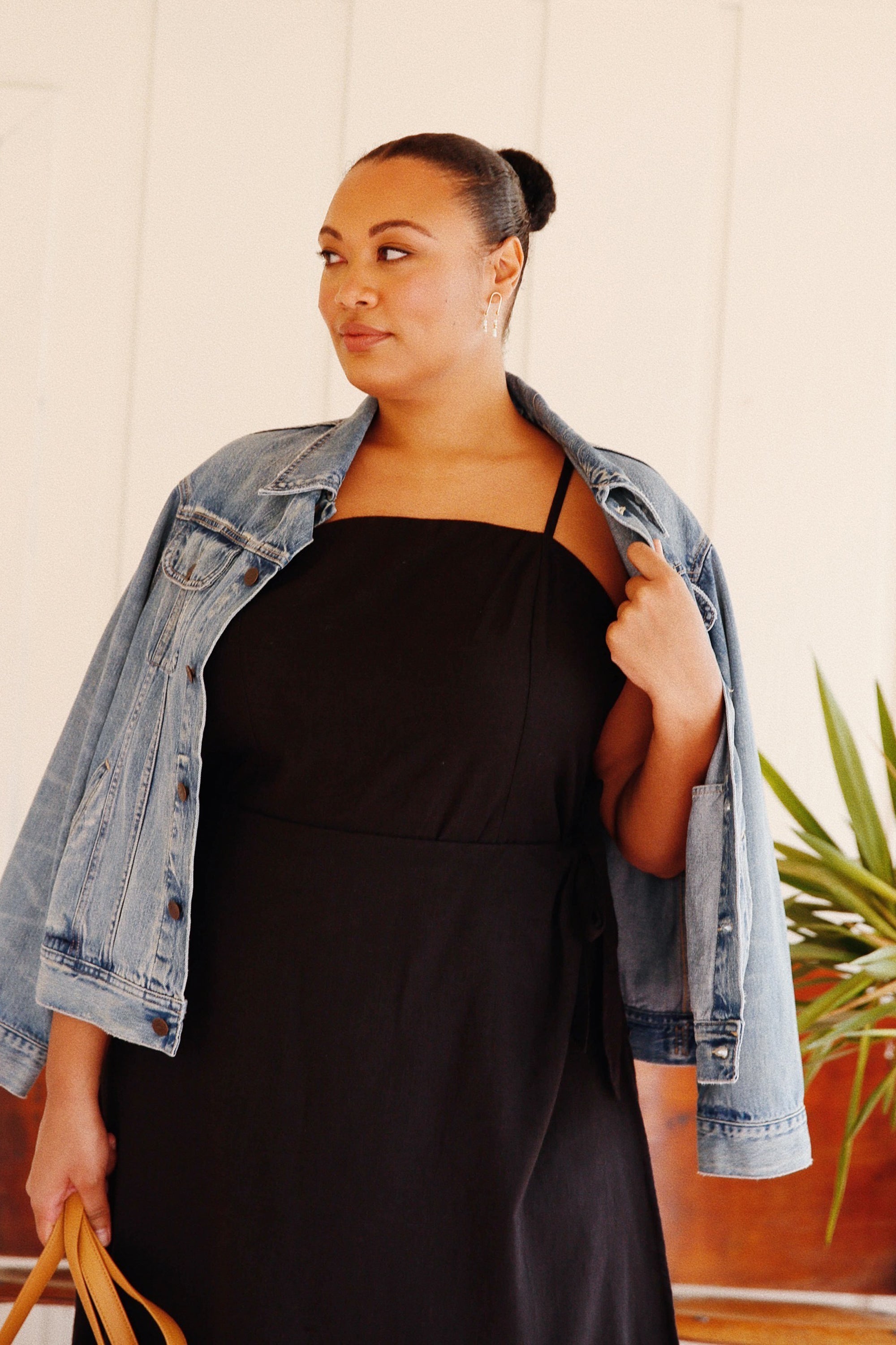 A woman in a black dress and denim jacket with a confident expression.