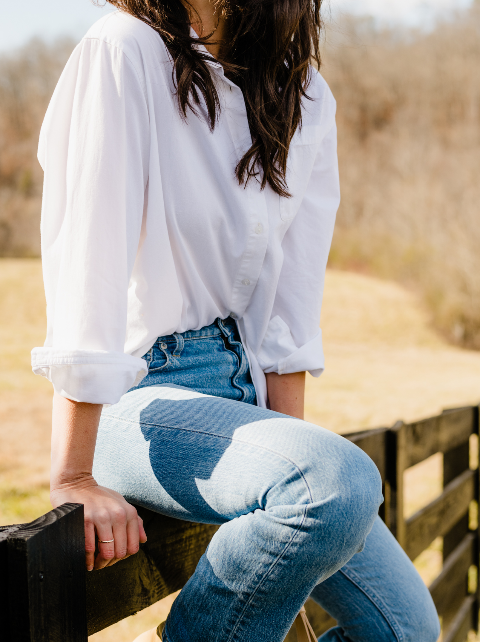 Woman in white blouse and blue jeans sitting on a wooden fence.