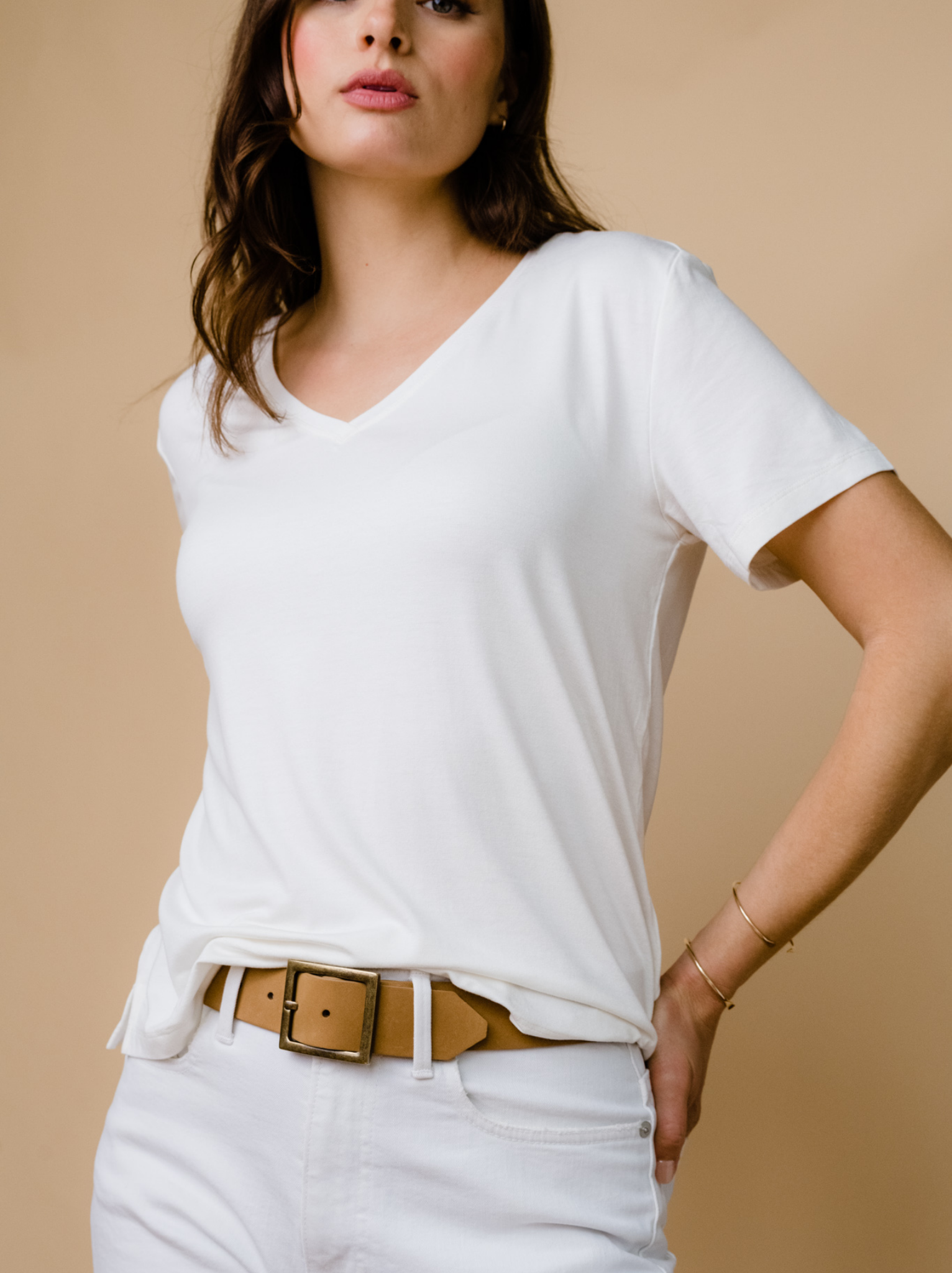 Woman in white outfit with a tucked-in V-neck T-shirt and tan belt.