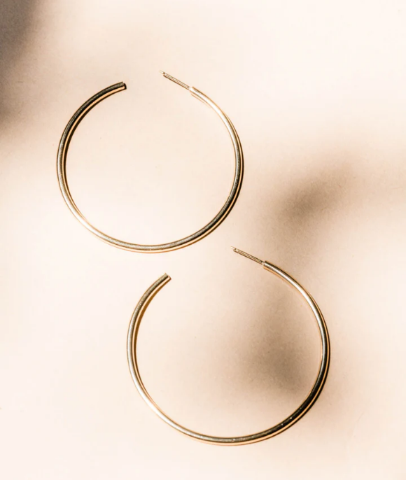 A pair of gold hoop earrings on a beige background.