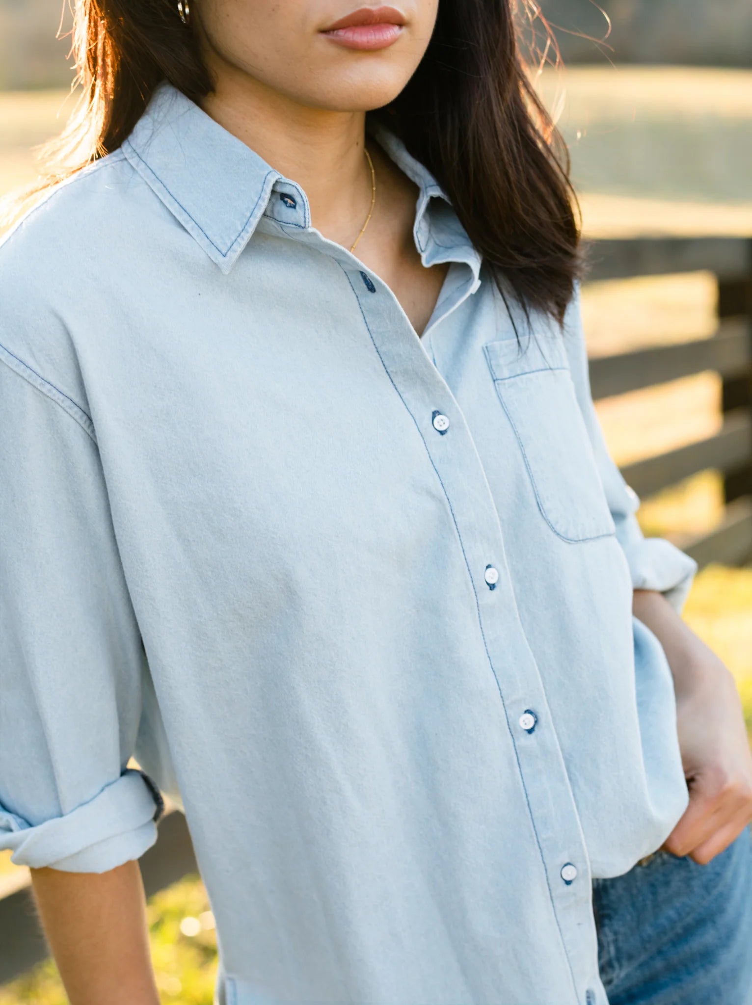'Cropped image of a woman in a blue denim shirt, partial face visible.'