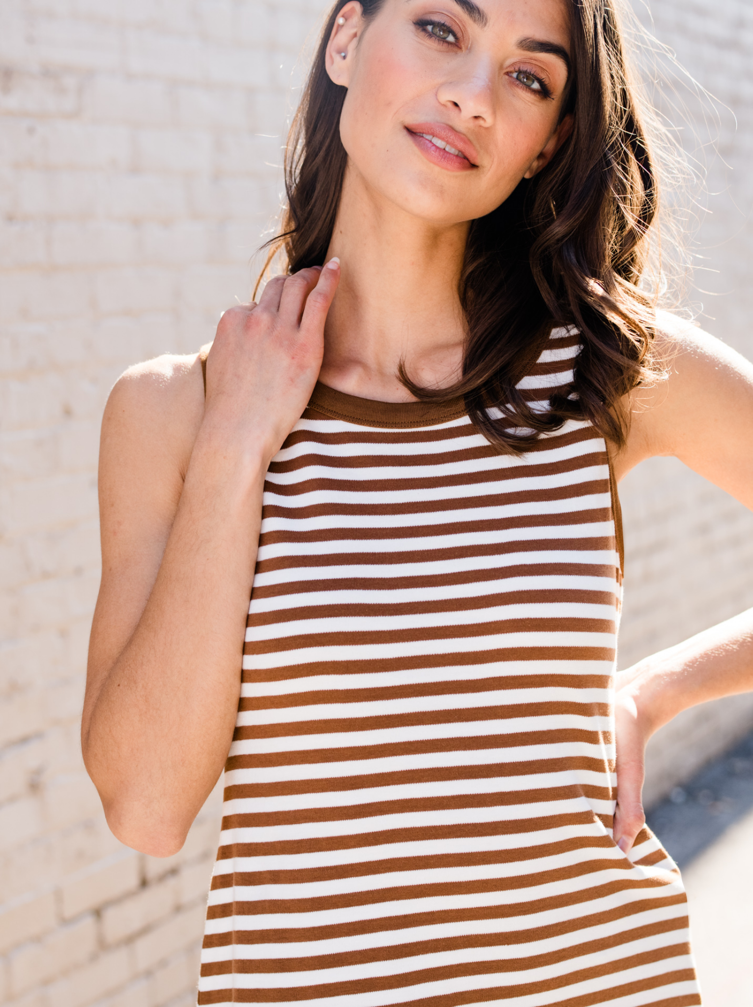 Woman in a striped dress standing against a white brick wall.