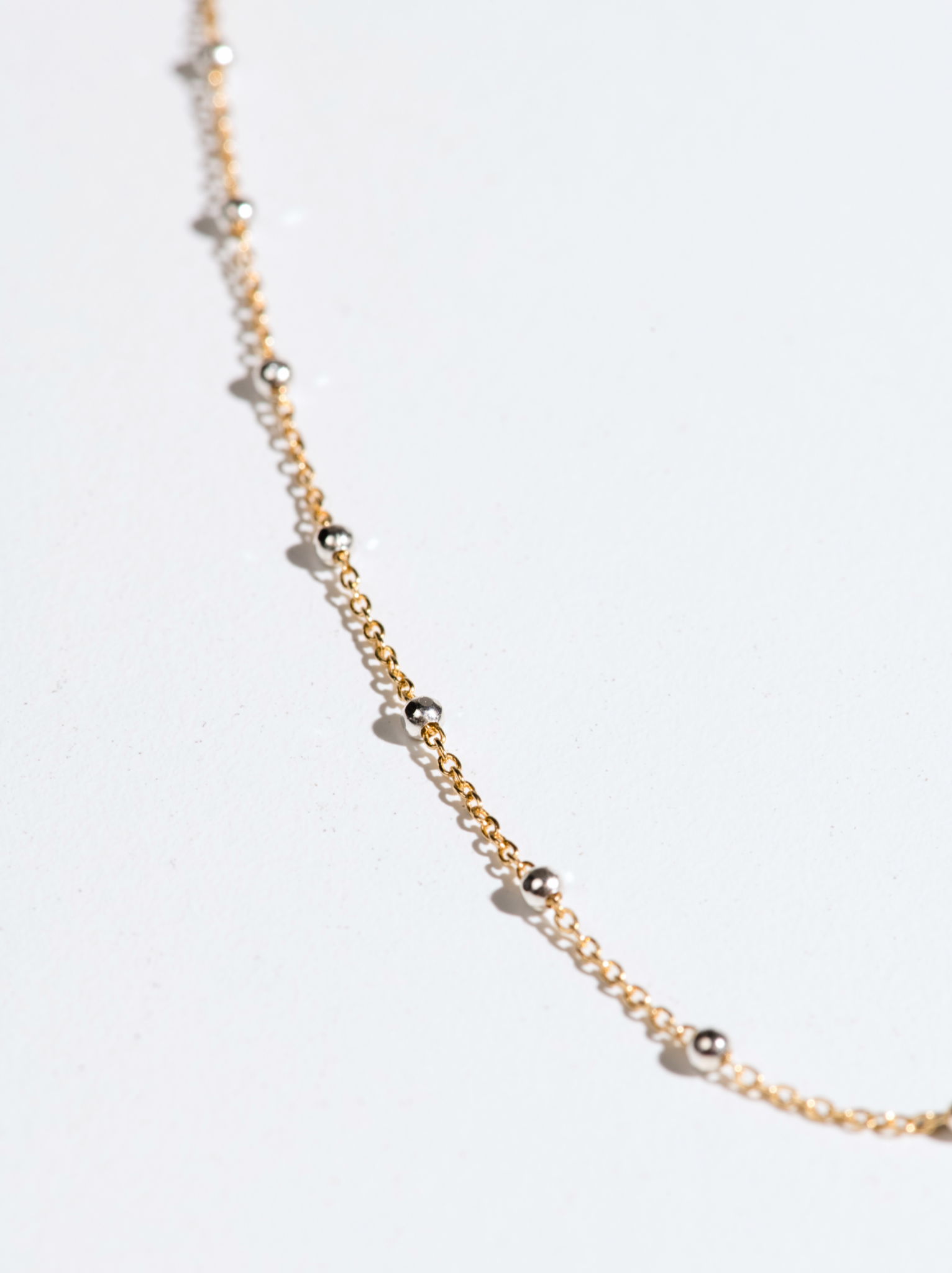 A delicate gold chain with small silver beads on a light background.