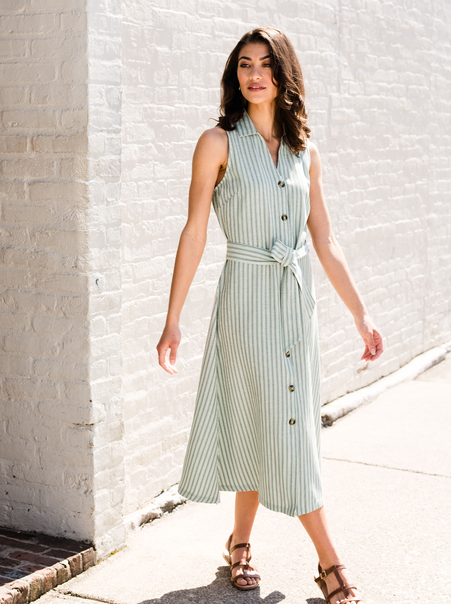 Woman in a sleeveless striped dress standing against a white brick wall.