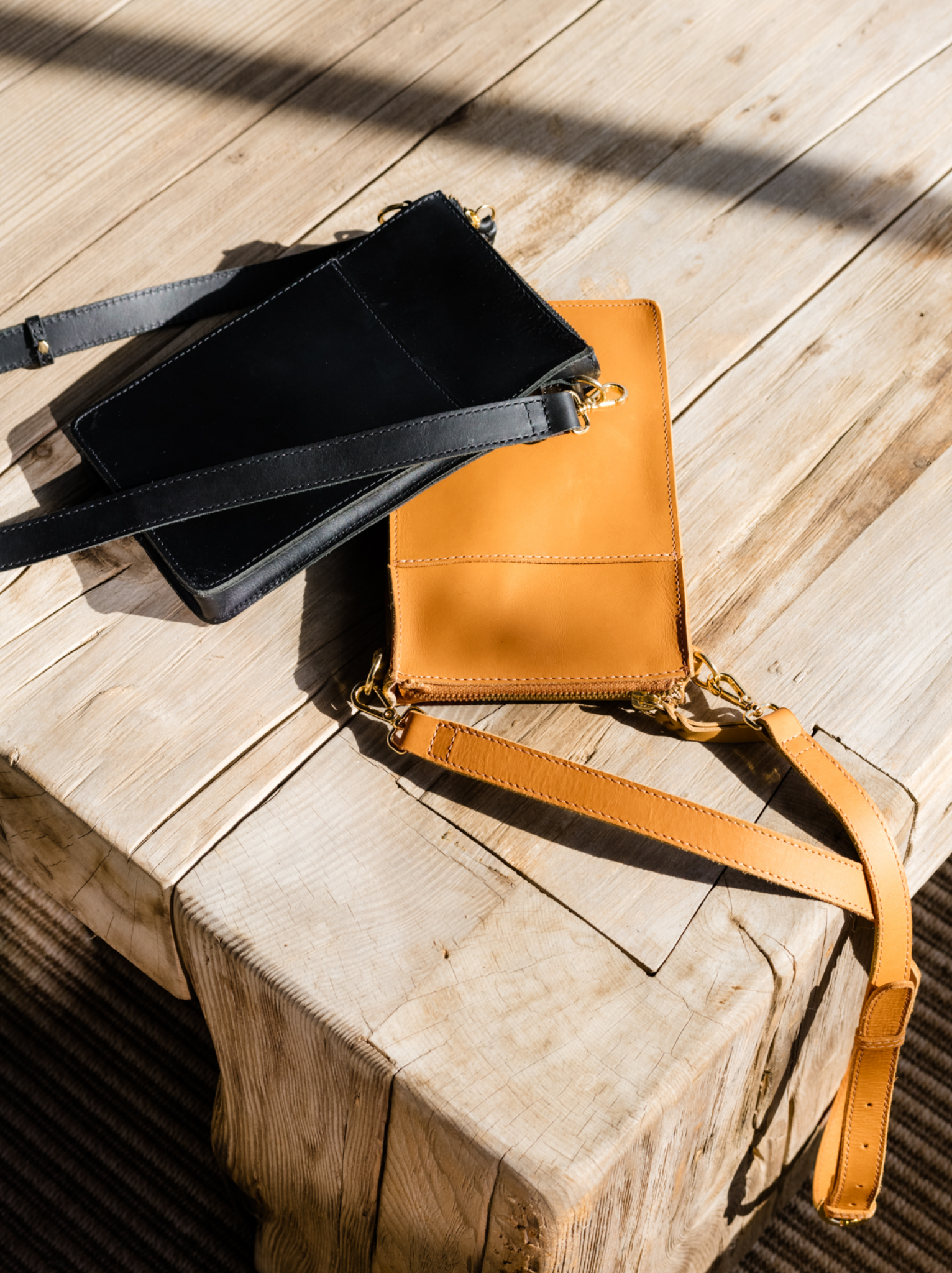 Two crossbody bags on a wooden stump in sunlight.