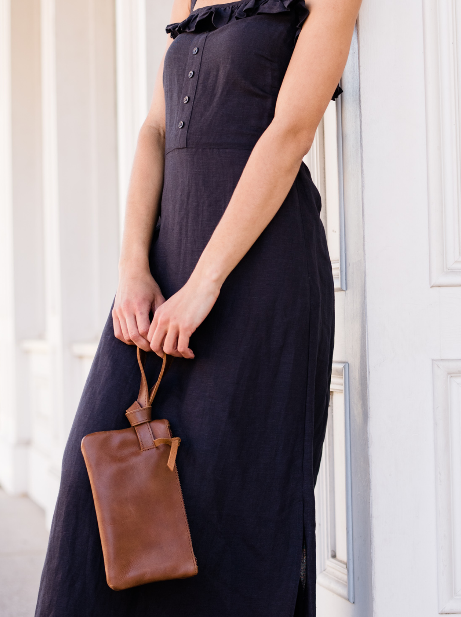 Woman in a navy dress holding a brown leather clutch.