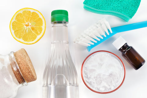 Glass bottles filled with clear liquid, scrub brush and other cleaning supplies on white background