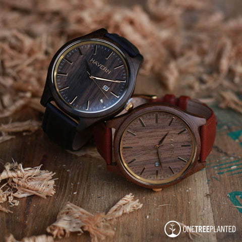 two leather band wooden watches laying on a whiskey barrel top