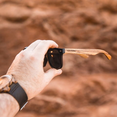 wooden sunglasses being held up by man with watch on