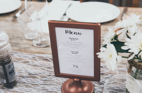 A copper-colored sign with the menu of a meal at a wedding reception is displayed on the table.