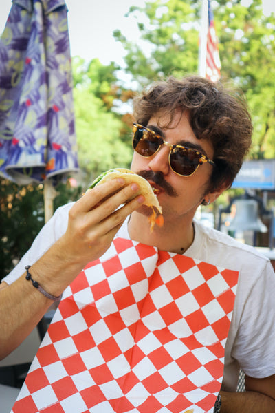 A man eating a taco wearing a Red & White Diamond NEATsheet, a disposable clothing protector with easy-to-use adhesive tabs.
