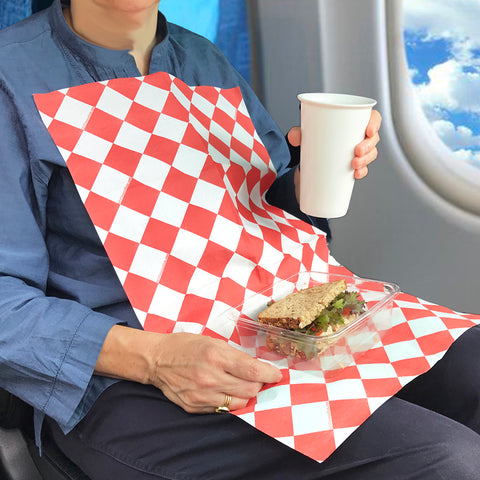 Woman on a plane with a sandwich and drink wearing a red and white diamond NEATsheet.