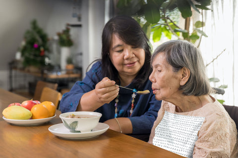 Elderly woman being served soup while wearing a Grey Dot NEATsheet.