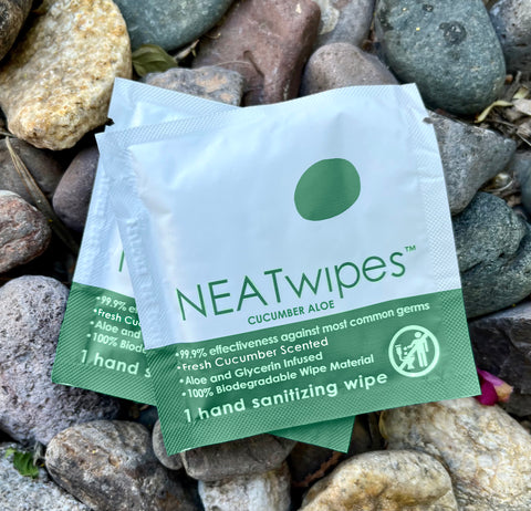 An individually wrapped NEATwipes Cucumber Aloe hand wipe on top of rocks.