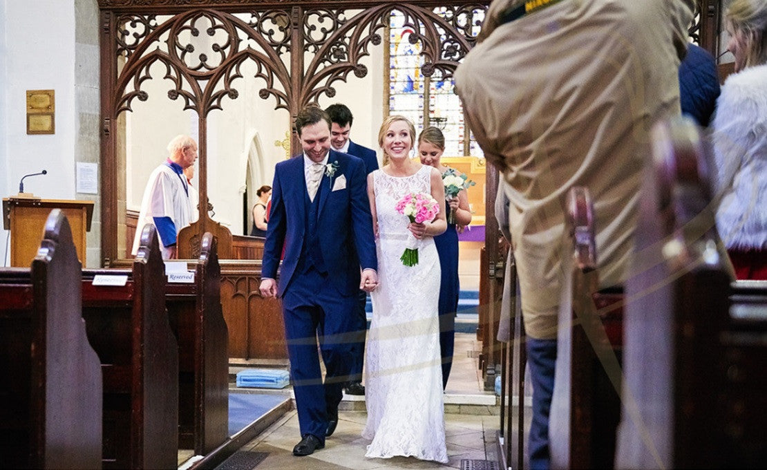 Wedding couple walking down church isle with wedding bouquet and buttonhole.