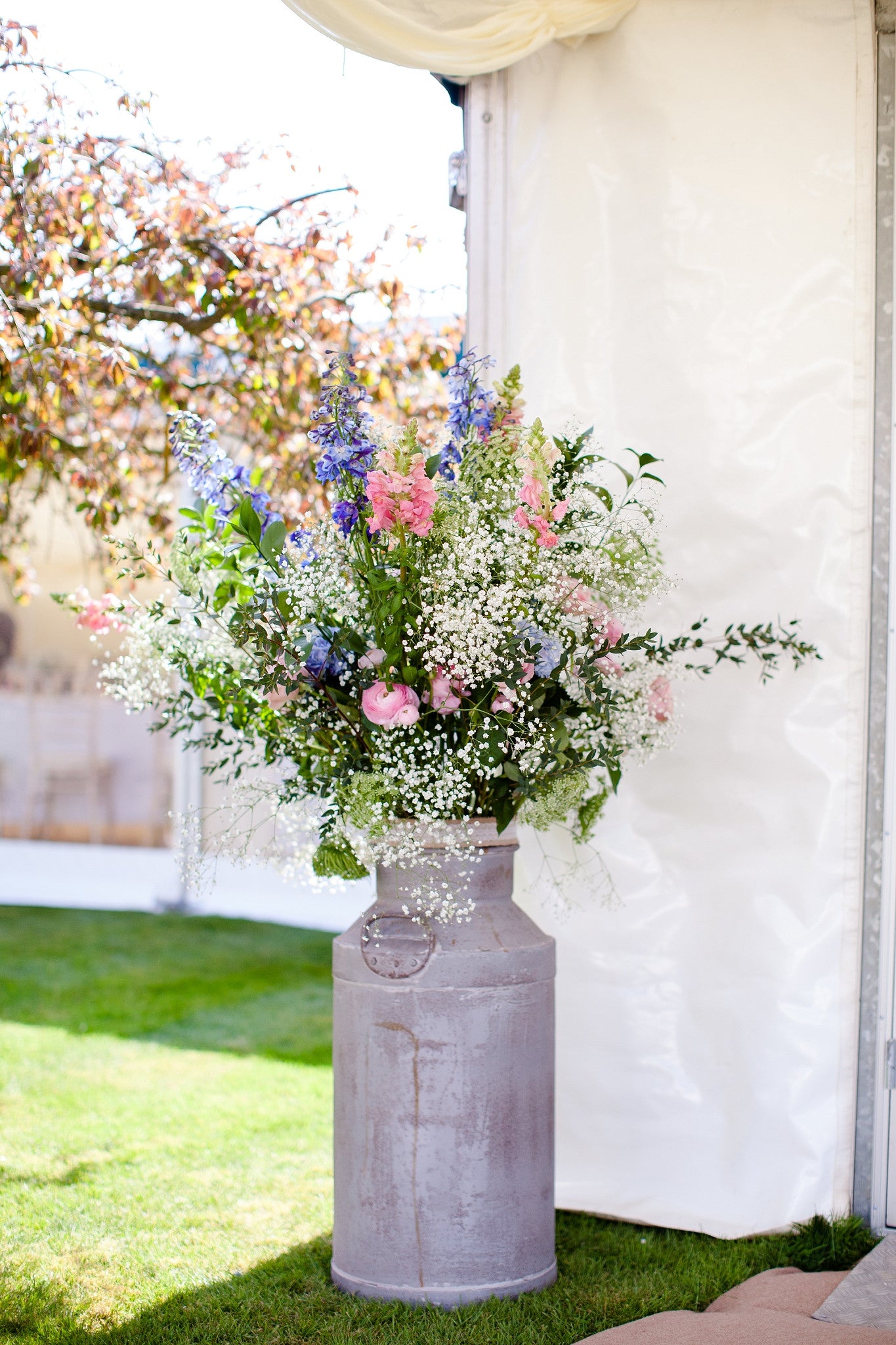 Milk churn based wedding floral arrangement with Gypsophila and flowers in shades of blue and pink.