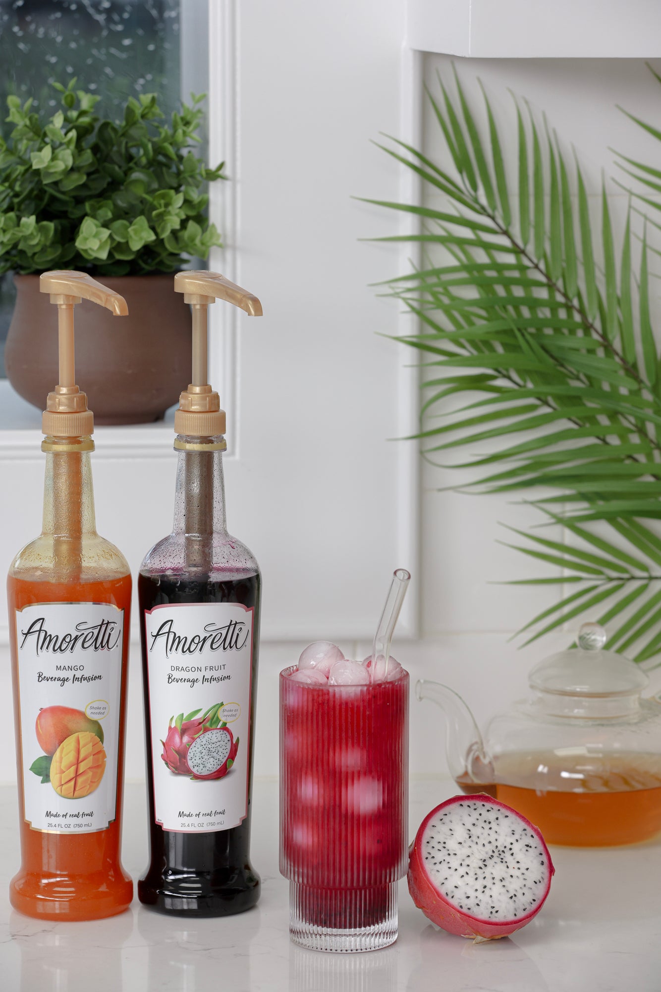 Amoretti Mango Beverage Infusion, Amoretti Dragon Fruit Beverage Infusion next to Dragon Fruit Tea with fresh dragon fruit next to a tea pot of green tea and palm leaves sitting on a kitchen counter